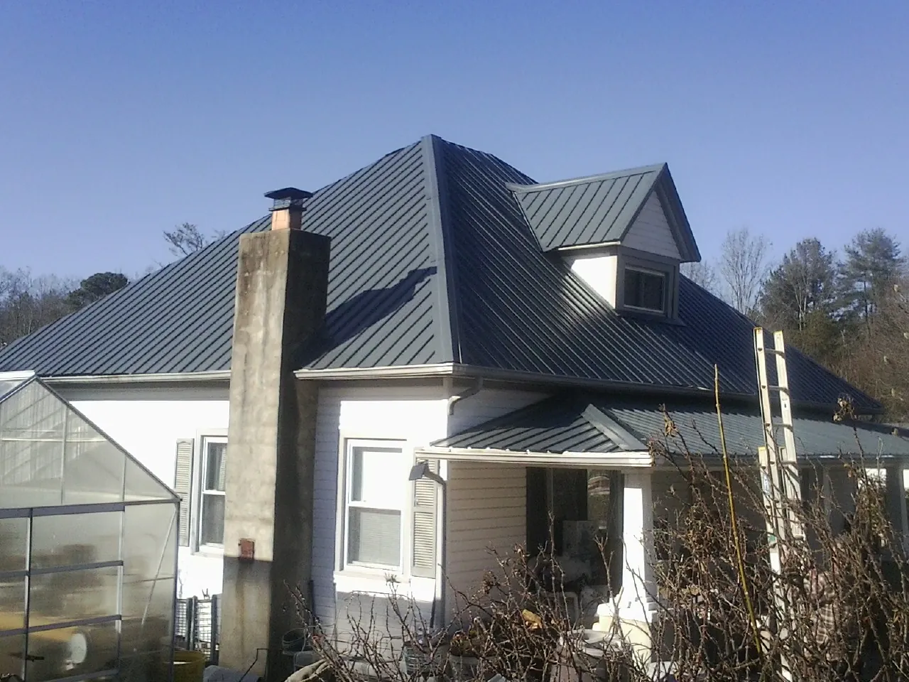 Dark blue standing seam metal roof on a white farmhouse with dormer — Slate & Tile Roof Repair by Roofing Brothers in Ethel