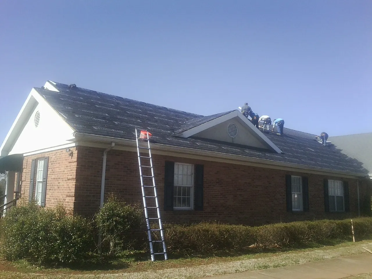 Crew tearing shingles off a brick ranch roof with a ladder set — Emergency Roof Repair work by our crew in Ethel