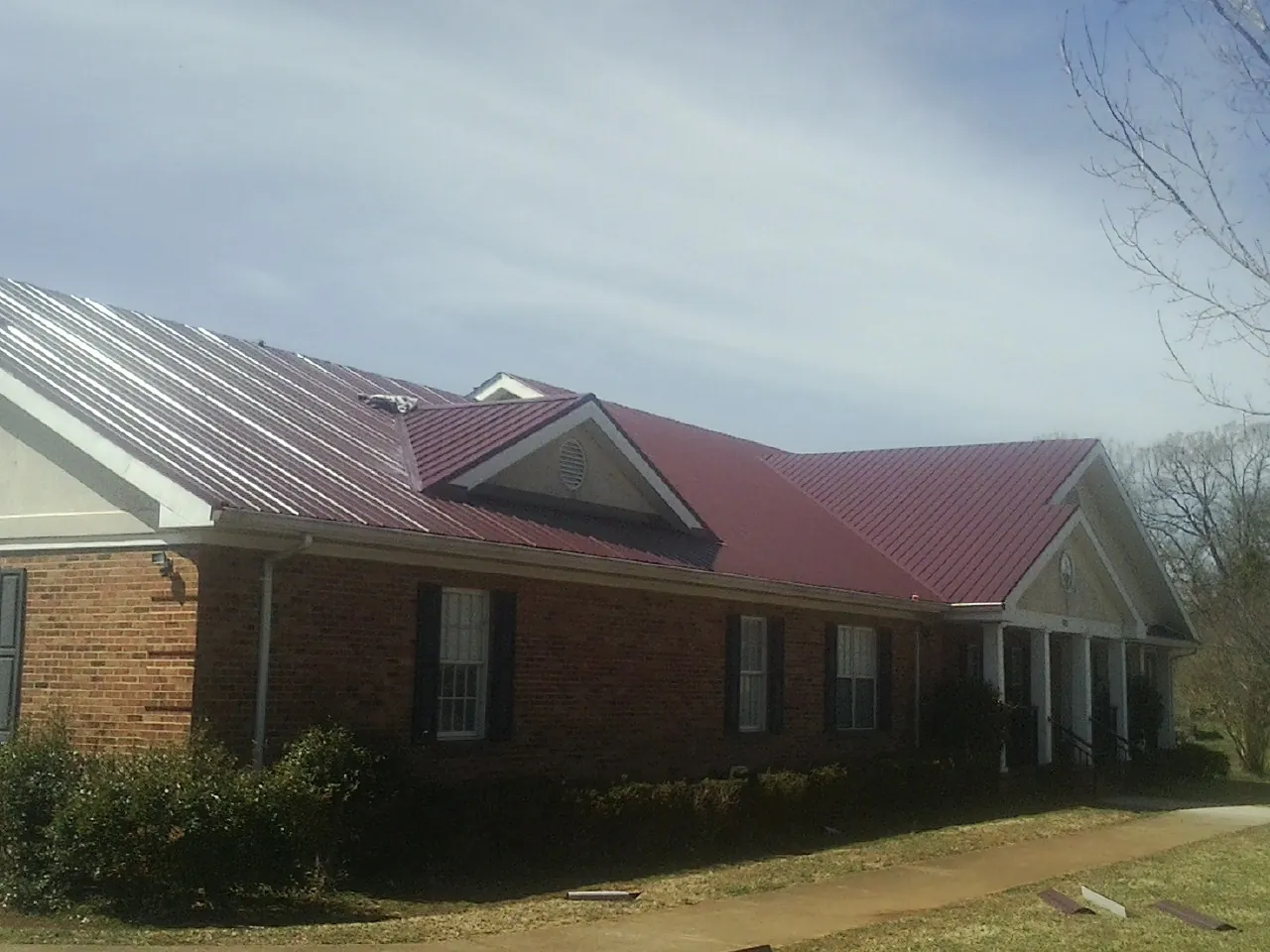 Red metal roof with gabled entries on a long brick building, from a Hail Damage Roof Repair job in Ethel