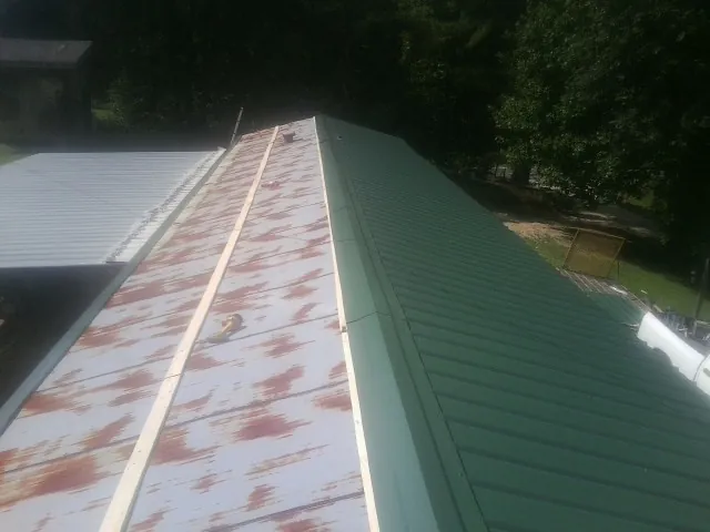 Old rusted panels beside newly installed green metal roofing — Wind Damage Roof Repair by Roofing Brothers in Ethel