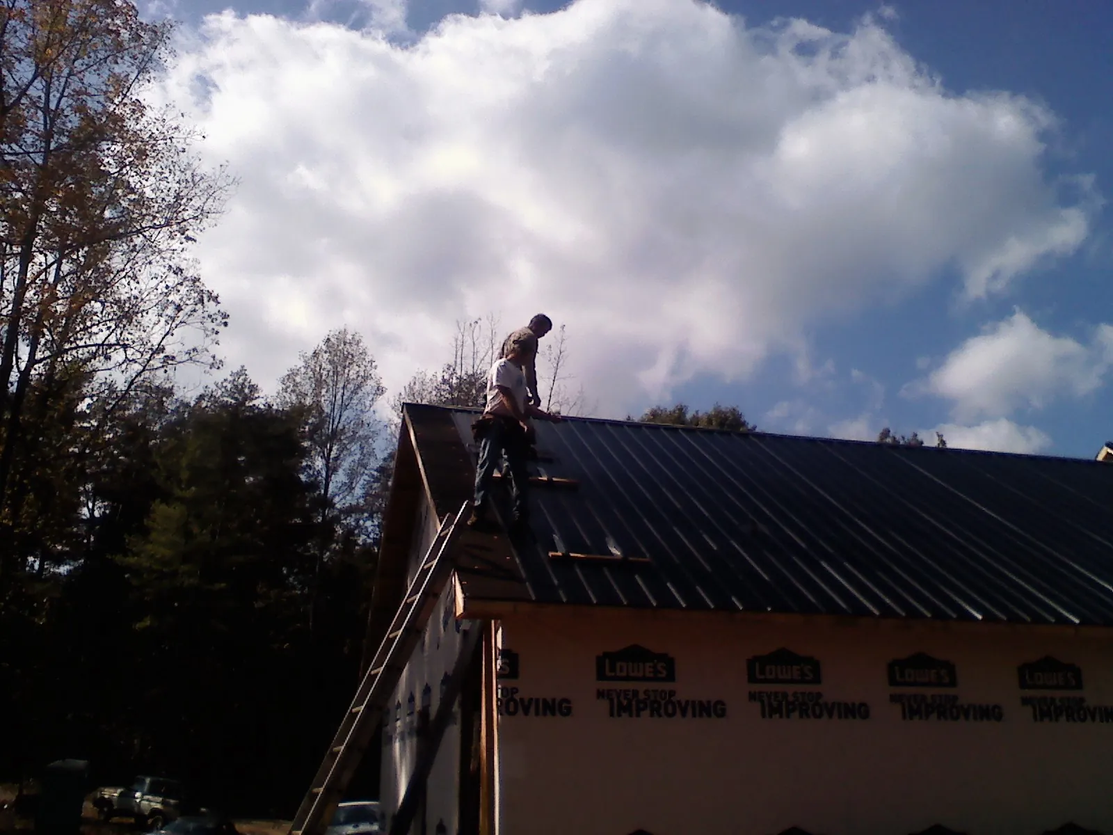 Roofer fastening dark metal panels high against a cloudy sky, from a Roof Inspection job in Ethel