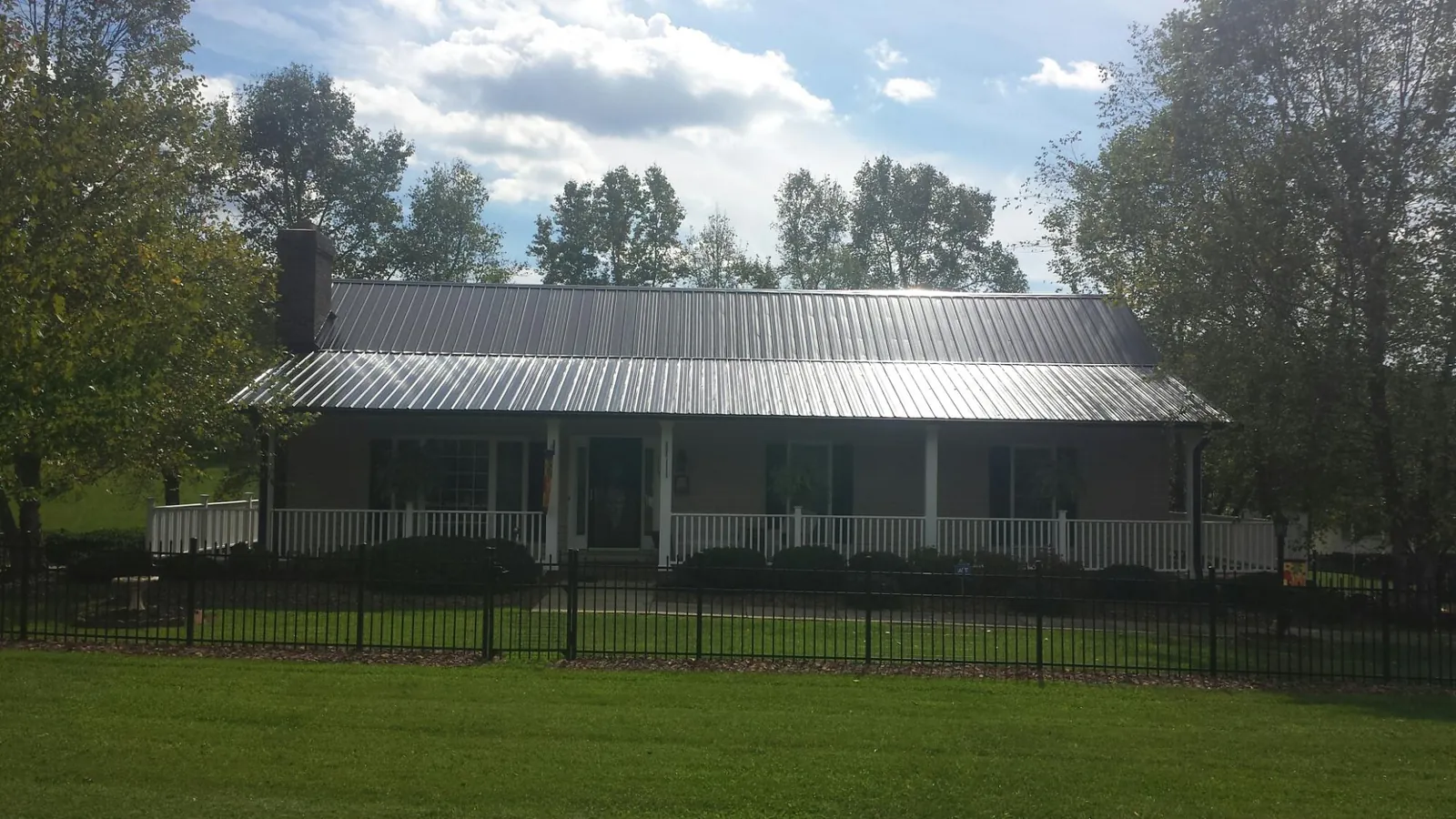 Gray metal roof on a brick ranch with a full width front porch — Gutter Guard Installation work by our crew in Ethel