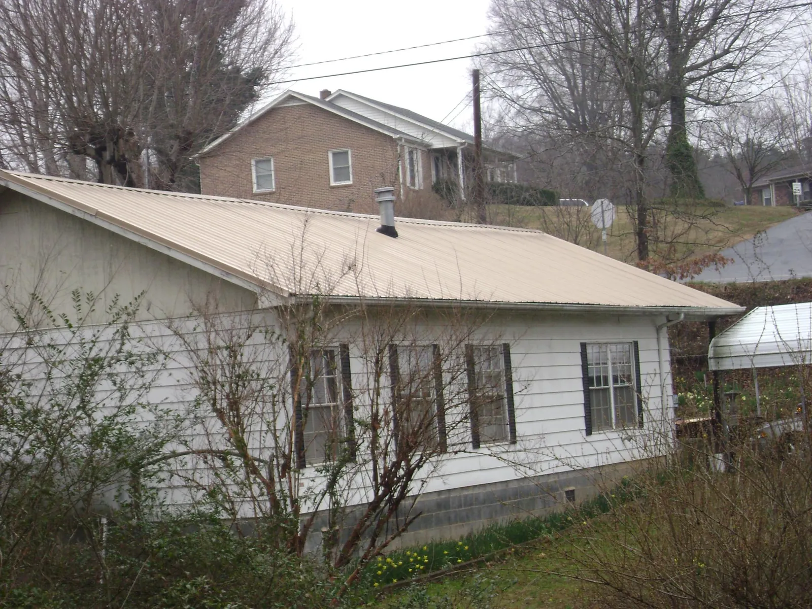 Tan metal roof on a white sided house set into a hillside — Commercial Roofing by Roofing Brothers in Ethel