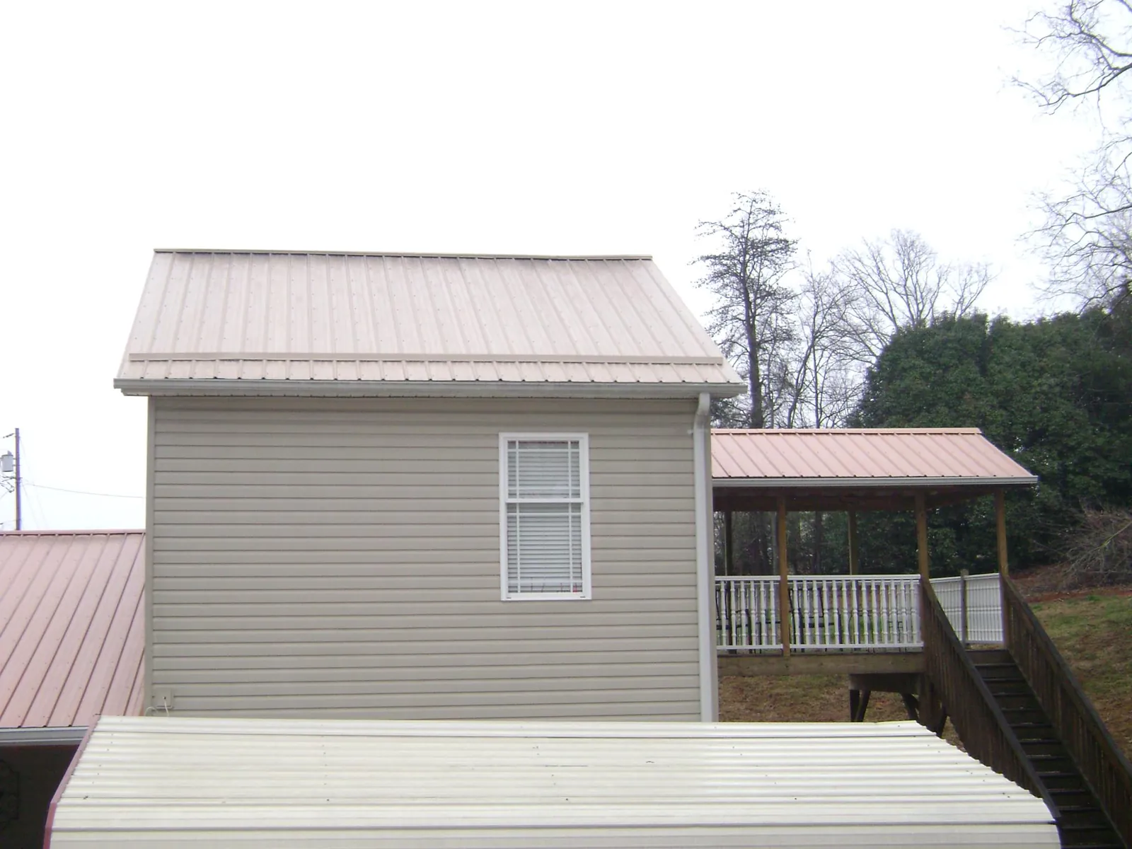 Tan metal roofs on a two story addition and attached porch, from a Roof Replacement job in Ethel